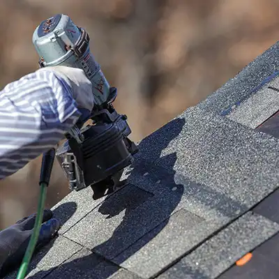 Worker installing new gray shingles on a roof with a nail gun